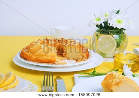 Yellow summer table setting with lemon bundt cake white plates teapot and chrysanthemum flowers in a glass vase