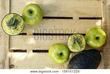 Wooden background with organic green detox smoothie made of avocado apple and banana with chia and leaves of mint and fresh fruits. Selective focus.
