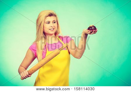 Diet sweets cooking baking food concept. Woman holding rolling pin and delicious chocolate cupcake with peanut frosting. Studio shot on blue background