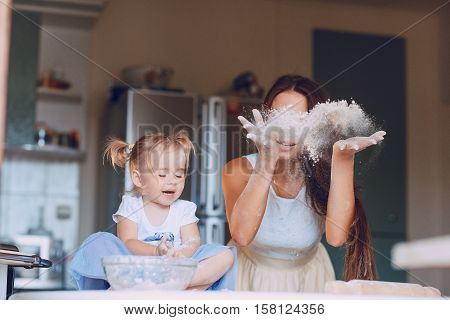 young beautiful mother teaches daughter prepare dough in the kitchen