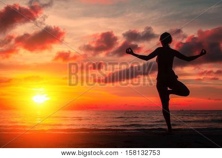 Silhouette young woman practicing yoga on the beach at surrealistic bloody red sunset.