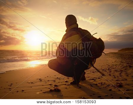 Man sit at evening sea. Hiker with backpack sit in squatting possition along beach. Vintage Style Toned effect