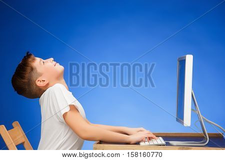 School-age boy sitting in front of the monitor laptop at blue studio backgroubd