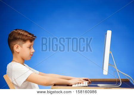 School-age boy sitting in front of the monitor laptop at blue studio backgroubd