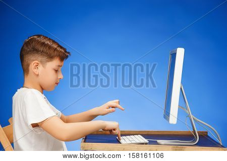 School-age boy sitting in front of the monitor laptop at blue studio backgroubd