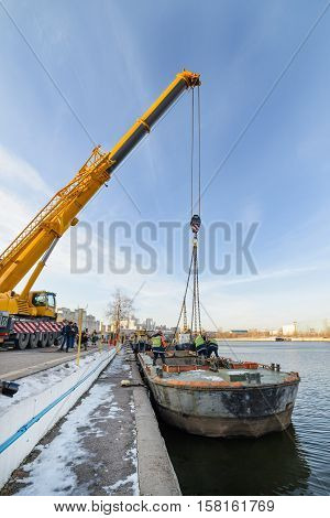 MOSCOW, RUSSIA - NOVEMBER 11, 2016: State Unitary Enterprise Mosvodostok performs recovery vessels on coastal winter parking. Dockers slings to lift the barge from the river.