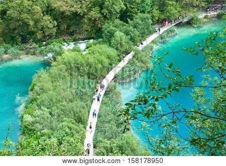 Tourists walking along a hiking path among two ponds with turquoise water. View from above. Plitvice lakes national park Croatia