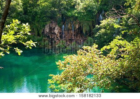 Lake with transparent emerald water. Waterfall among red rocks and foliage. Plitvice lakes national park Croatia