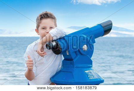 Boy near the scoping public binocular telescope (binoscope) near the sea in Spain. Travel concept.