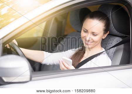 Young smiling woman looking at her phone screen traveling by car, using navigation app to find way