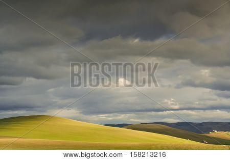 RURAL LANDSCAPE WINTER.Between Apulia and Basilicata. Hilly landscape with farmhouse dominated by thunderclouds. -ITALY- .Play of light on cultivated field dominated by thunderclouds.