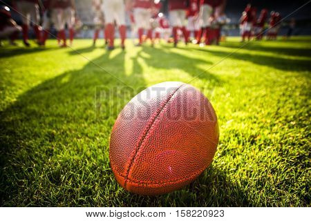 close up of an american football on the field, players in the background