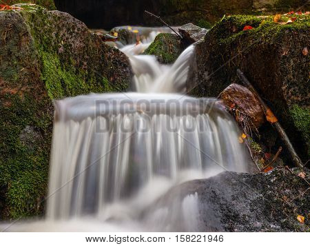 Autumnal mood in the forest with small creek waterfalls. Long exposure shot with blurred silky water stream.