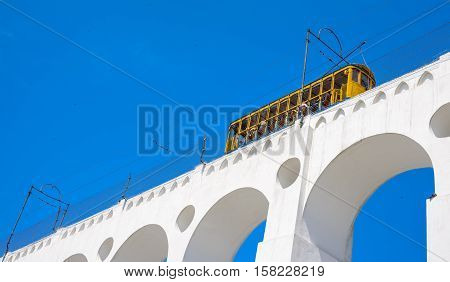 Tram of Santa Tereza, Bonde de Santa Teresa, drives along distinctive white arches, Arcos da Lapa, of the landmark in historic district of Rio de Janeiro - Brazil.