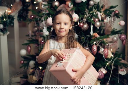 Little cute girl in dress standing near christmas tree and holding gifts. New year. Vintage toned
