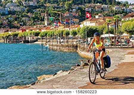 Ascona Switzerland - August 23 2016: Woman riding a bicycle at the promenade at the luxurious resort in Ascona on Lake Maggiore in Ticino canton in Switzerland.