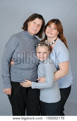 Child with her mother and grandmother on a gray background.