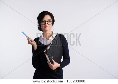Young Caucasian woman wearing a dark blue dresst and and a white shirt, holding a ring binder folder and pen. Isolated on light background