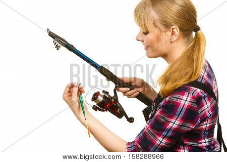 Fishing concept. Attractive woman in dungarees pink check shirt holding and looking at rod. Isolated background