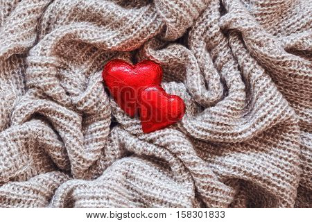 Closeup macro texture of knitted wool fabric material with red candy hearts on top clothing background with wrinkles and folds Valentine holiday card love concept