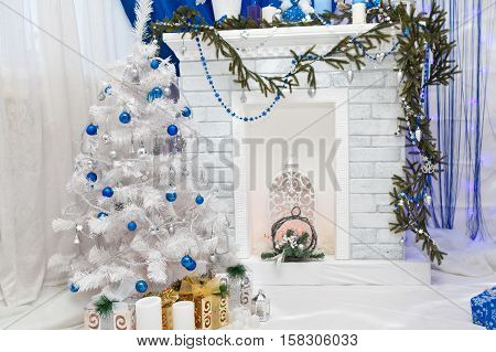 Fireplace and snow-covered Christmas tree with blue Christmas balls in a festive beautiful interior