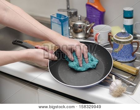 Houseproud woman washing a frying pan in her messy kitchen cropped selective focus shot