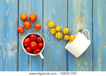two white cups with redyellow and orange tomatoes pouring them onto a blue wooden textured background
