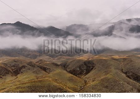 Scenic autumn view on the hills and mountain slopes with sparse vegetation fog and clouds on a background cloudy sky