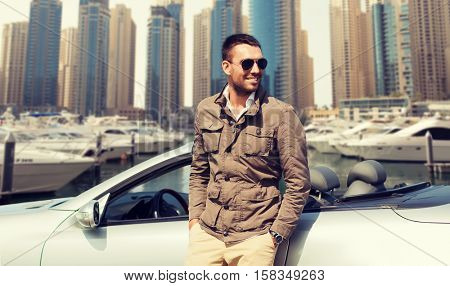 auto business, transport, leisure and people concept - happy man near cabriolet car over dubai city port background