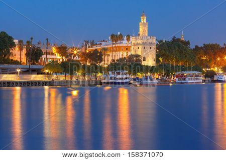Dodecagonal military watchtower Golden Tower or Torre del Oro and Guadalquivir river during evening blue hour, Seville, Andalusia, Spain