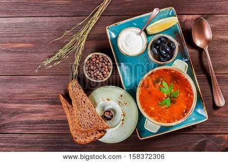Soup with meat olives herbs lemon sour cream in bowl black bread and spices on dark wooden background homemade food. Traditional Russian soup - solyanka. Top view