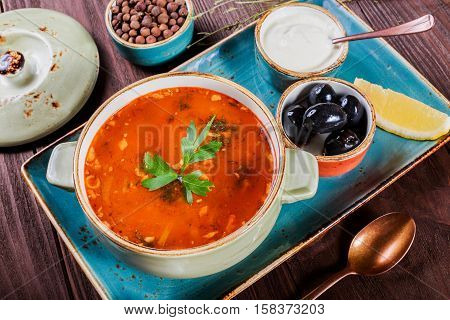 Soup with meat olives herbs lemon sour cream in bowl black bread and spices on dark wooden background homemade food. Traditional Russian soup - solyanka. Top view