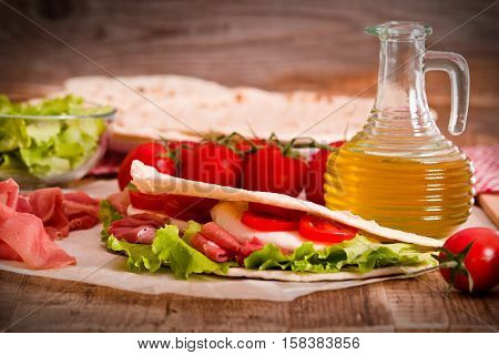 Piadina with ham and lettuce on wooden table.