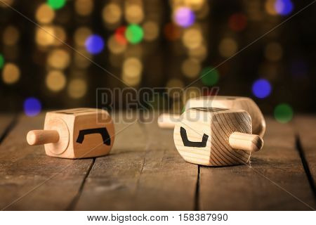 Dreidels for Hanukkah on wooden table against defocused lights