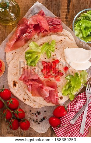 Piadina with ham and lettuce on wooden table.