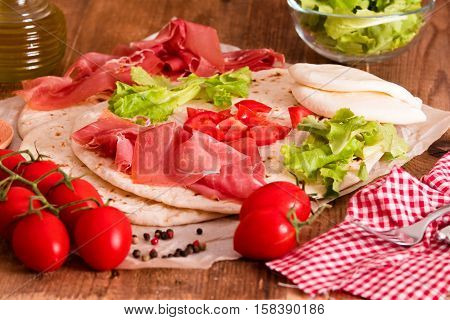 Piadina with ham and lettuce on wooden table.