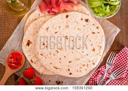 Piadina with ham and lettuce on wooden table.