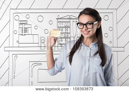 Time to buy something. Pretty young cheerful girl wearing glasses and holding shopping discount card while smiling.