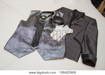 Wedding dress, tie, belt, gloves, vest, and suit lying on a bed