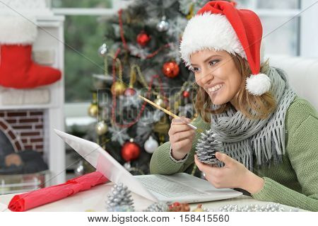 Portrait of young smiling woman in Santa hat preparing for Christmas, making hand made decoration