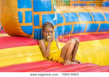 Girl Eats An Apple Sitting On The Edge Of The Inflatable Trampoline In Amusement Park