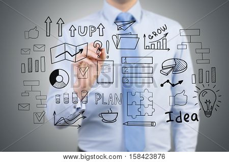 Close up of a businessman in a blue shirt who is drawing a startup idea sketch on a glassboard.
