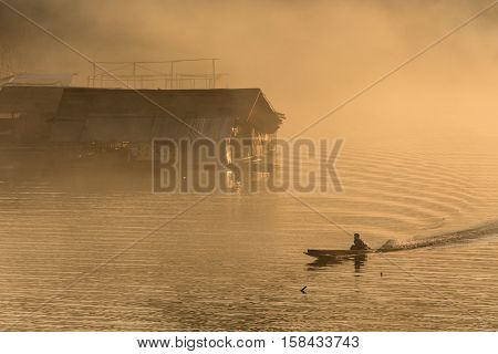Misty tropical sunset on lake with boat and wooden home in Sangklaburi, Thailand