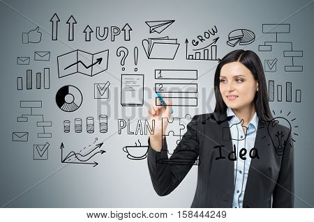 Close up of a businesswoman with black hair who is drawing a startup idea sketch on a glassboard.