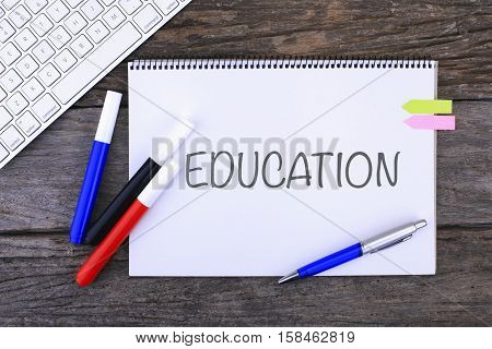 Notebook with EDUCATION Handwritten on wooden background and Modern Computer Keyboard. Top View Composition