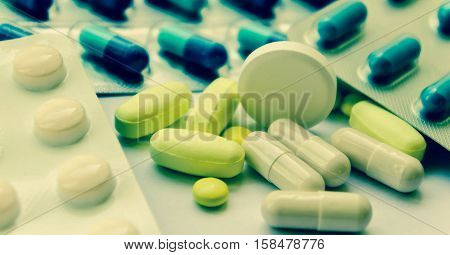 medical pills white, yellow and blue, small and one big round on the right of the photo, medicines in packing and scattered on a white table, yellow oblong heap lie, processed, preset,