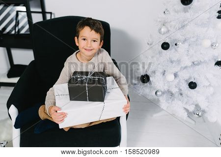 boy sitting on a chair near a Christmas tree with Christmas presents