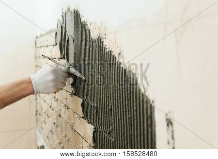 Installing the tiles on the wall. A worker setting tiles in the form of brick. He put adhesive using a comb trowel.