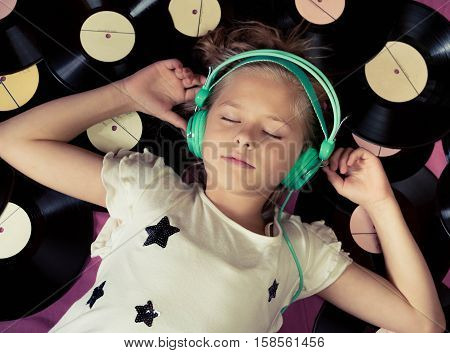Beautiful girl lying next to vinyl records and listening to music on headphones. Top view.