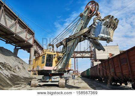 heavy excavator loading gravel into train for rail freightage